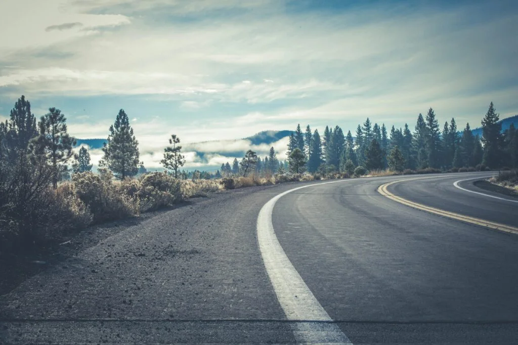 A scenic view of a winding highway through a conifer forest on a cloudy day, offering natural beauty.